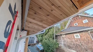Cedar porch ceiling with an unfinished light opening and a neighbouring building beyond