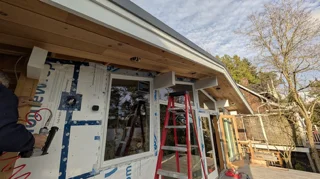 Exterior porch with cedar soffit, windows, construction wrap and a red ladder