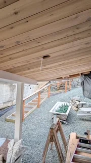 Covered exterior walkway with a cedar ceiling, posts and a railing beside garden steps